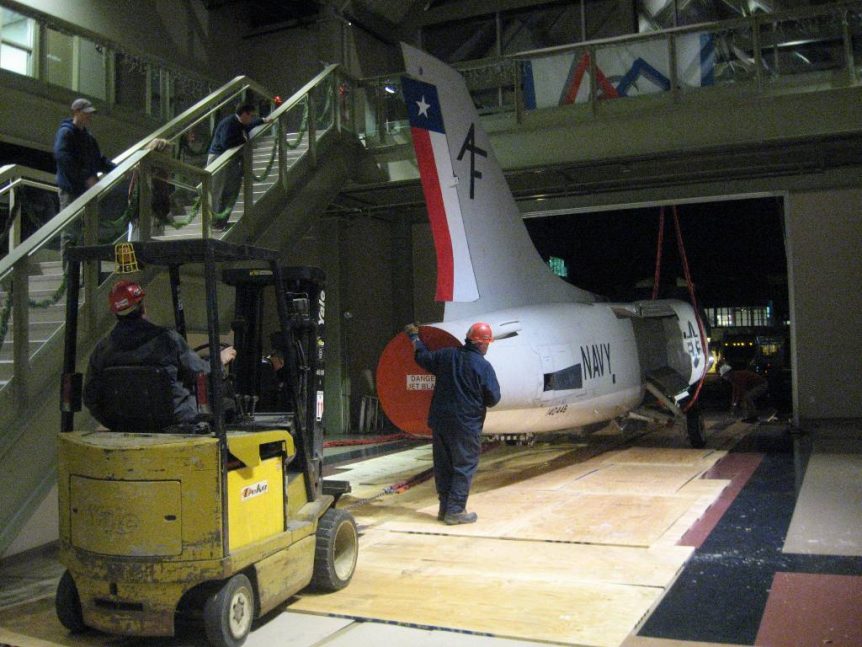 Louis P. Cote, Inc.'s riggers use a crane and forklift to position the body of a 1956 U.S. Navy XF8U-2 Crusader jet inside of the McAuliffe-Shepard Discovery Center in Concord NH